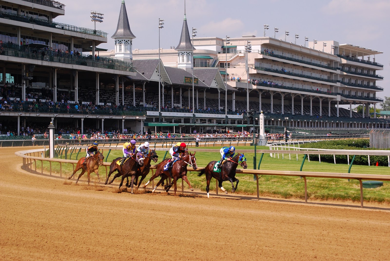 Open dirt track and rails at Churchill Downs with the grandstand behind